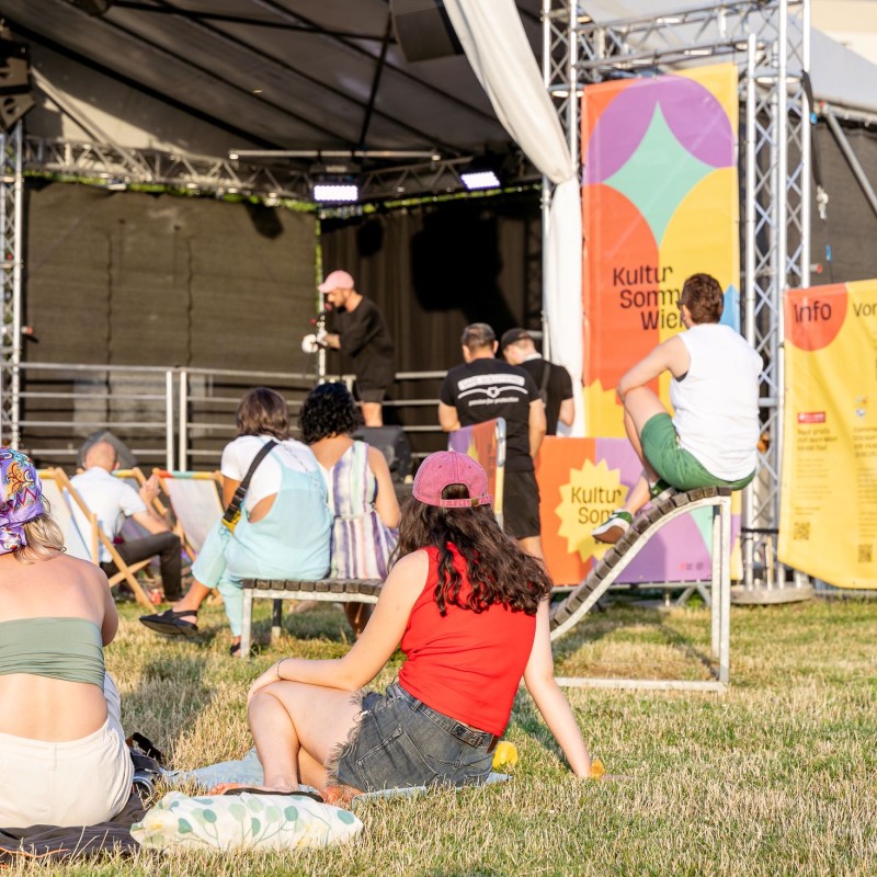 Bruman Rockner: Publikum sitzt vor der Bühne im Gras. Auf der Bühne sieht man Bruman Rockner.