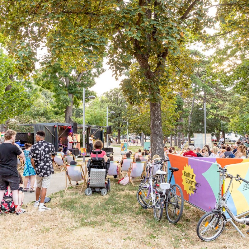 Deep Talk: Die Band Deep Talk steht auf der Bühne im Hyblerpark. Im Vordergrund stehen Fahrräder. Das Publikum sitzt in Liegestühlen und auf Decken am Boden.