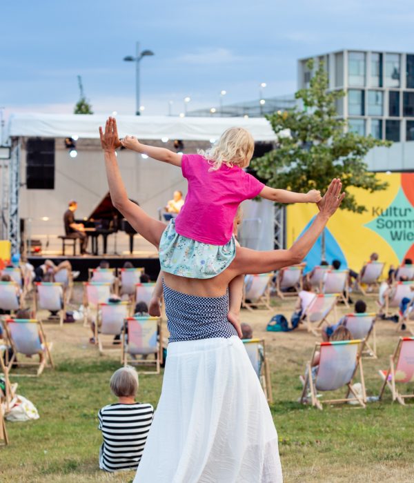 Frau mit Kind auf den Schultern tanzt vor der Bühne bei der Seestad Aspern